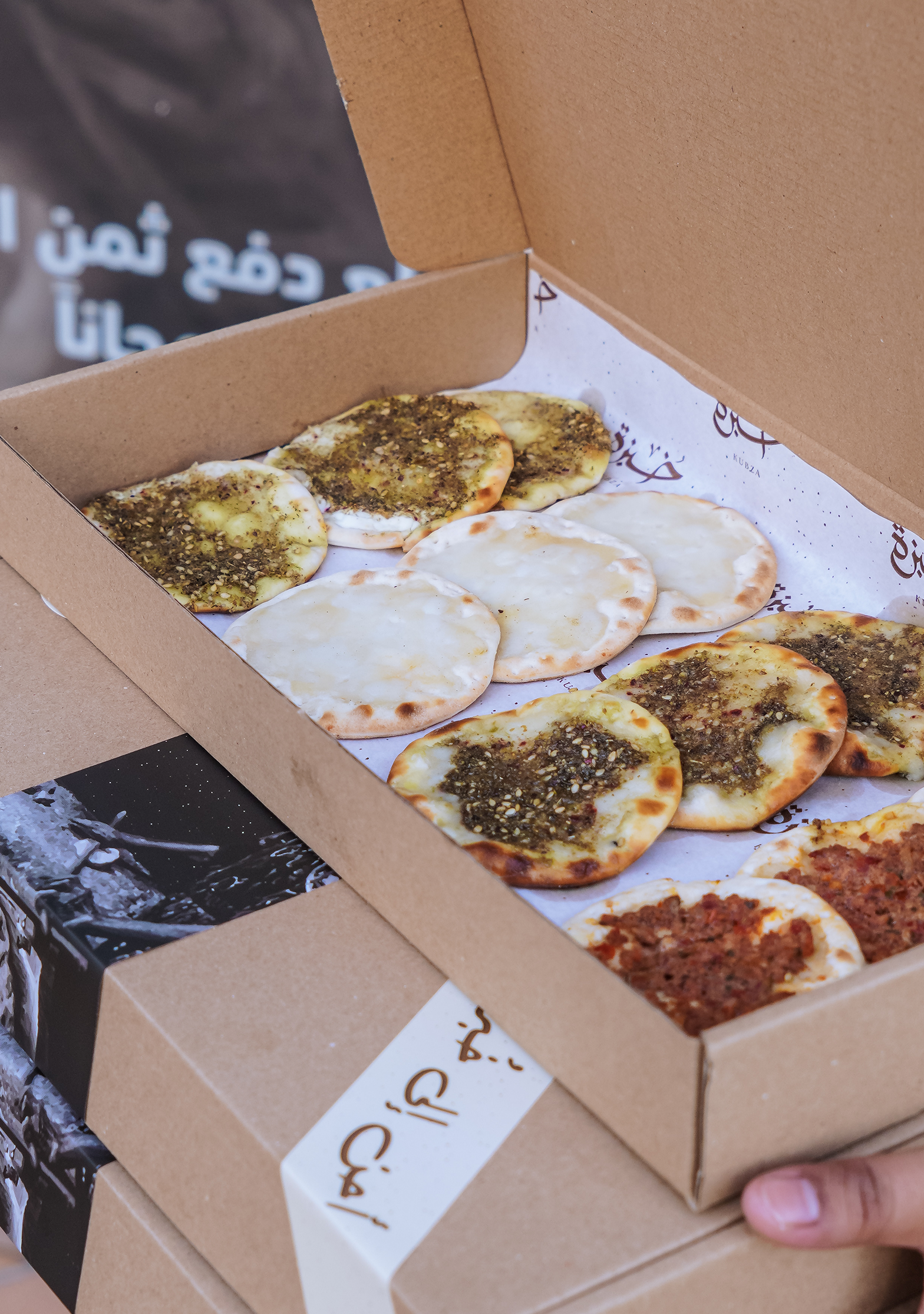Kraft box from Khubza filled with assorted mini manakish topped with zaatar, cheese, and meat, neatly arranged on branded paper